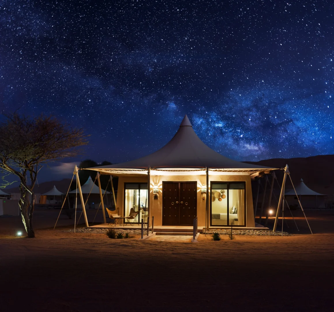 Illuminated exterior of a Premier Villa at Desert Nights Resort Oman at night, set among the dunes of the Wahiba Sands desert